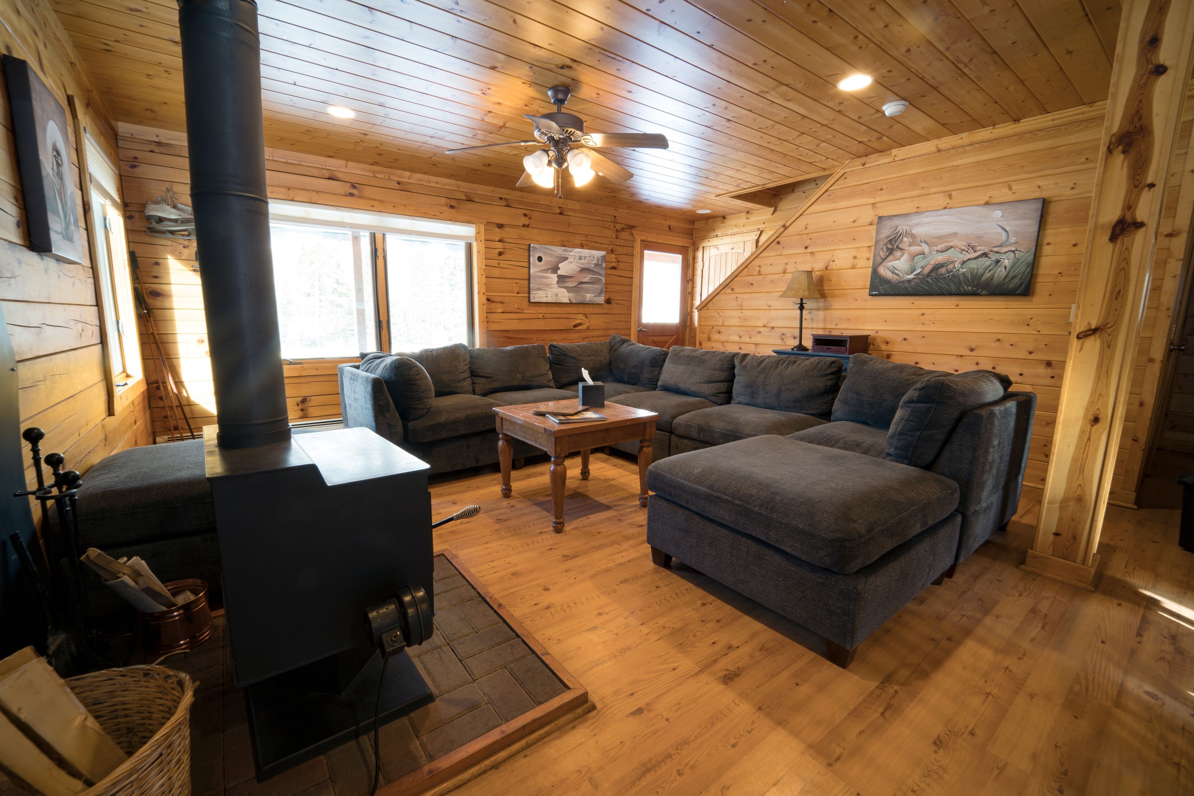 Ein gemütliches Blockhaus-Interieur mit Kaminofen, Ecksofa und Deckenventilator.
