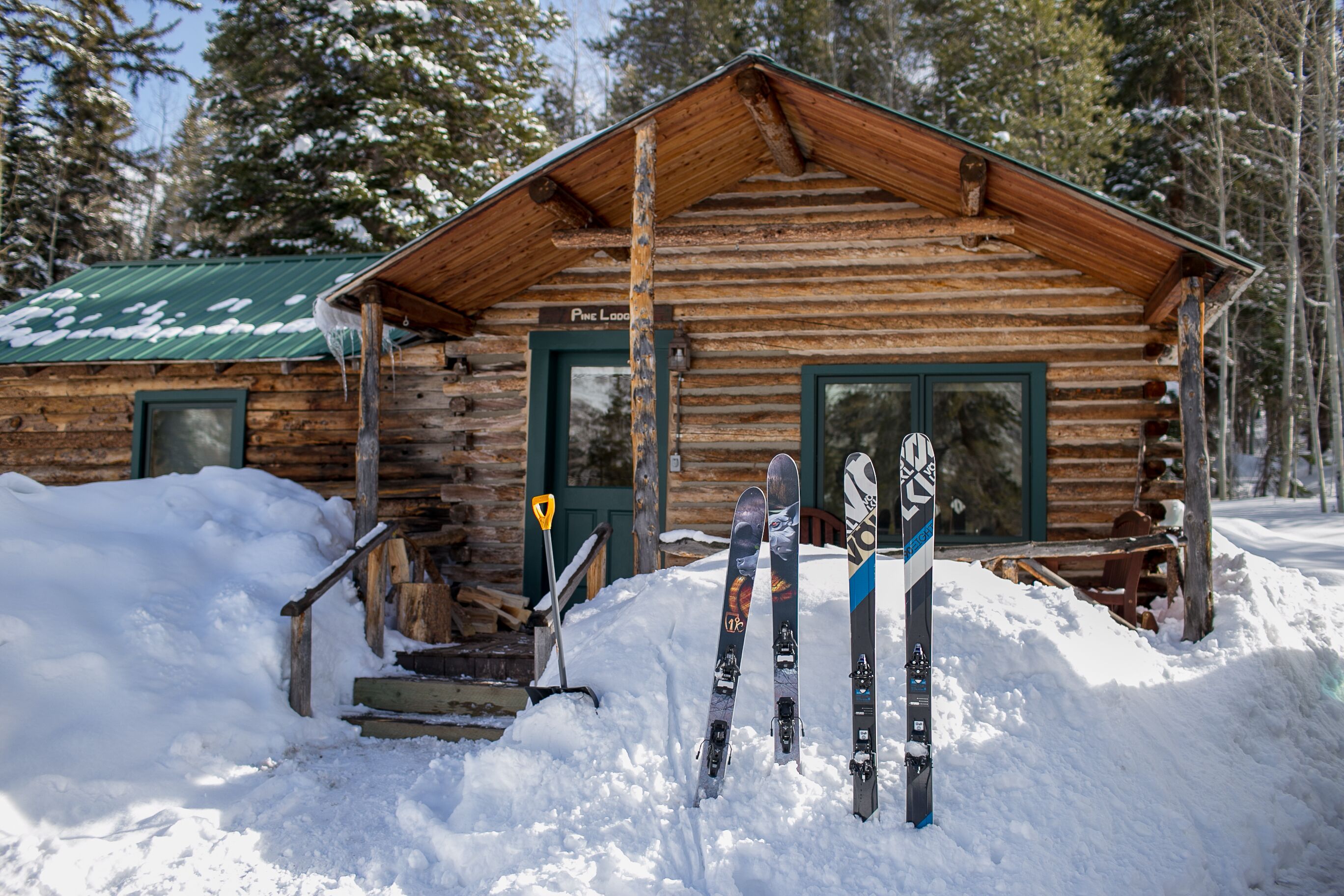 A rustic log cabin with a green door and windows, surrounded by snow.