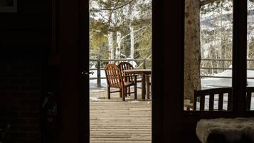 A wooden deck with a table and chairs, a bench, and a view of trees and snow outside.