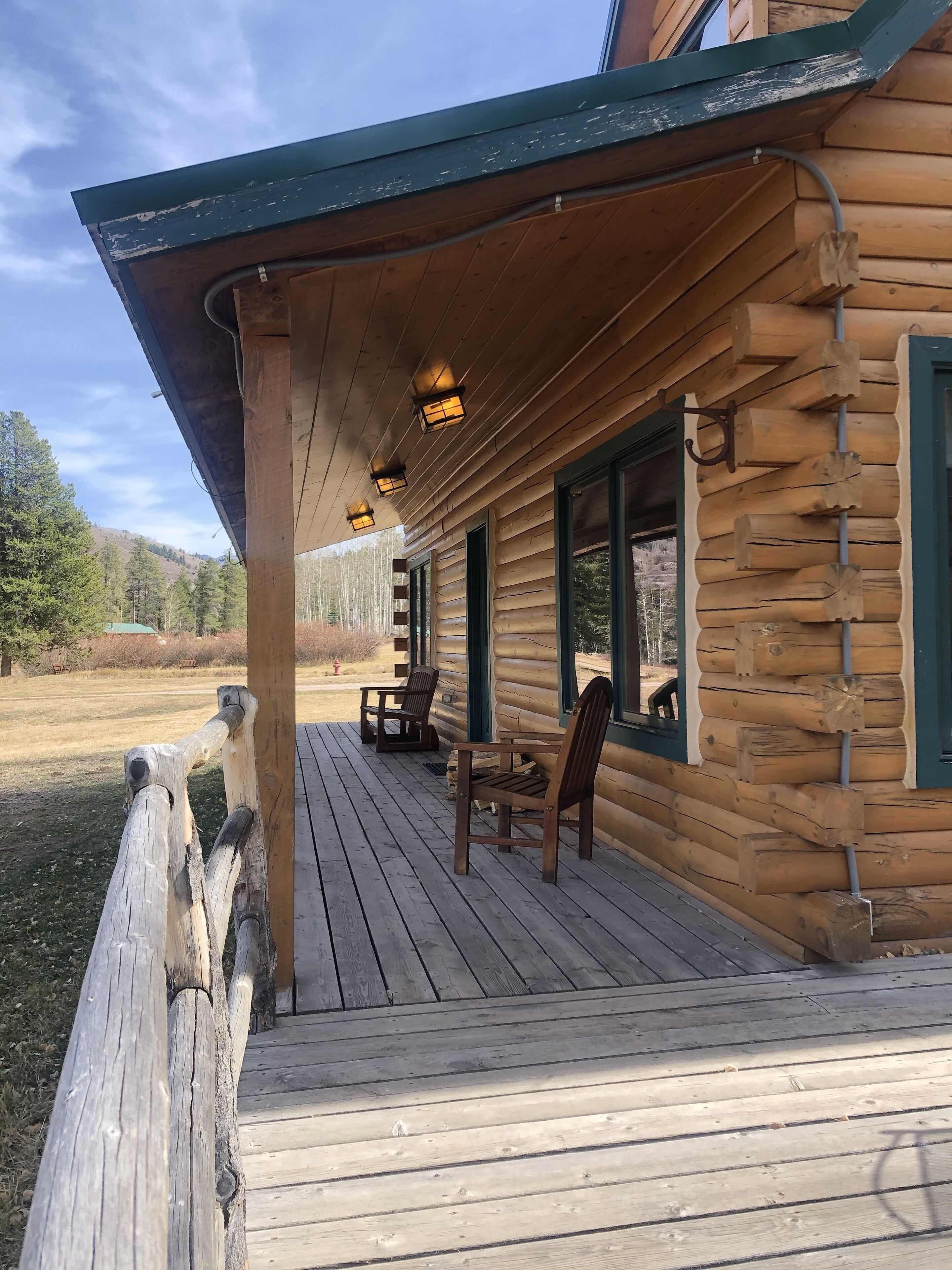 En stuga byggd av trä med en veranda, utomhusmöbler och utsikt över det omgivande landskapet.