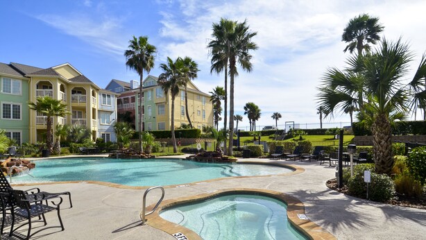A swimming pool area with multiple pools, lounge chairs, and palm trees. - The Dawn Beach Condos by AB Sea Resorts (Galveston)