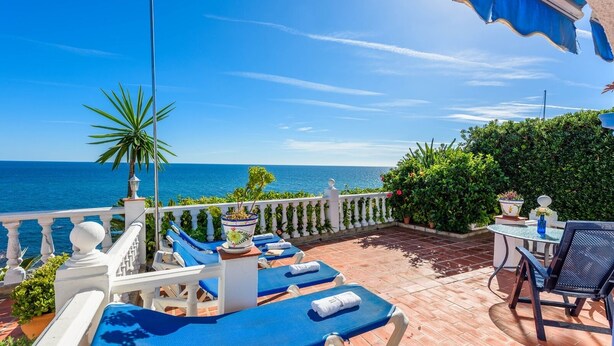 Una terraza con sillones azules, una mesa y vista al mar.