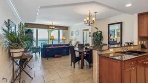 A spacious living area with a dining table, blue sofa, and potted plants. - 2B Gulf Front Tower 3 20th Floor - Stunning Views! (Pensacola Beach)