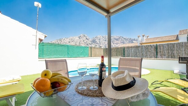 A table set outdoors with fruits, wine glasses, and a hat, overlooking a pool and mountains. - Camino de la Huerta Montejaque by Ruralidays (Málaga)