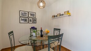 A dining area with a glass table, four chairs, a vase with flowers, a bottle of wine, and a fruit bowl. - Camino de la Huerta Montejaque by Ruralidays (Málaga)
