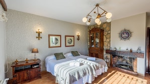 A bedroom with a large bed, a wooden dresser, a stone wall, a fireplace, and a chandelier. - Recreo San Andrés Ronda by Ruralidays (Málaga)