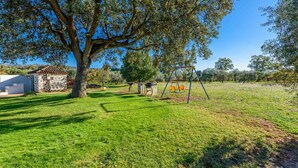 A grassy outdoor area with a swing set, a stone building, and a large tree. - Recreo San Andrés Ronda by Ruralidays (Málaga)