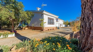 A white building with a tiled roof, a small garden with flowers, and a tree in the foreground. - Recreo San Andrés Ronda by Ruralidays (Málaga)