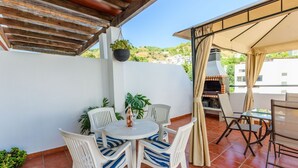 A patio with a round table and chairs, a hanging plant, and a grill area. - Casa Riu Tolox by Ruralidays (Málaga)