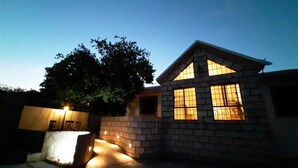 Una casa de dues plantes amb façana de maó, un finestral gran amb un disseny de reixa i un arbre al fons.