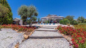 Ein Hotel mit einem im mediterranen Stil gestalteten Dach, einer überdachten Sitzgelegenheit im Freien und einem Kiesweg zum Eingang.