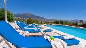 Ein Poolbereich mit Liegestühlen und Handtüchern, mit Blick auf die Berge im Hintergrund und einem gefliesten Pool.