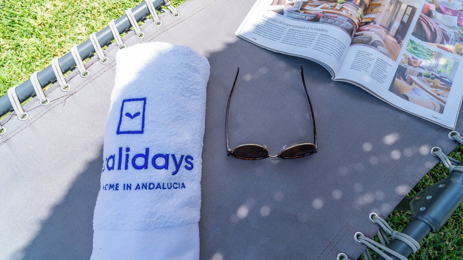 Een handdoek met de tekst 'adaildays' en 'COME IN ANDALUCIA', zonnebril en een tijdschrift op een mat.
