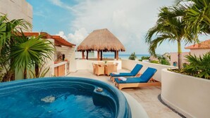 A rooftop pool area with lounge chairs, a thatched-roof structure, and a view of the ocean. - Ocean View 3 story Penthouse with private rooftop, jacuzzi, and balconies (Playa del Carmen)