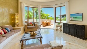 A spacious living room with a large window, a sofa, a coffee table, and a television. - Ocean View 3 story Penthouse with private rooftop, jacuzzi, and balconies (Playa del Carmen)