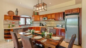 A modern kitchen with wooden cabinets, a stainless steel refrigerator, and a dining table set for four. - Ocean View 3 story Penthouse with private rooftop, jacuzzi, and balconies (Playa del Carmen)