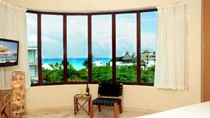 A hotel room with a large window offering a view of a beach and ocean. - Ocean View 3 story Penthouse with private rooftop, jacuzzi, and balconies (Playa del Carmen)