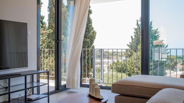 A modern room with a large TV, a sofa, and a balcony with a view of trees and buildings. - Capistrano Garden Nerja by Ruralidays (Málaga)