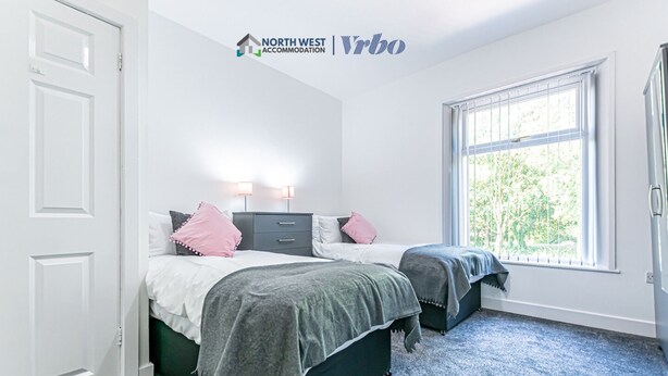 A bedroom with two beds, a window with blinds, a white door, and a carpeted floor.