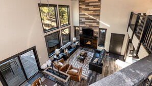 A spacious living area with a fireplace, large windows, and a ceiling fan.
