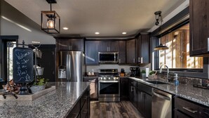 A modern kitchen with dark wood cabinets, stainless steel appliances, granite countertops, and a chalkboard with a welcome message.