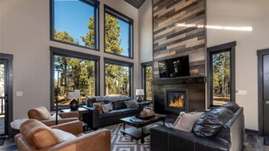 A spacious living room with large windows, a fireplace, and leather sofas.