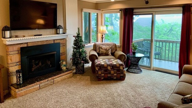 A living room with a fireplace, a television, a Christmas tree, and a balcony with outdoor furniture. - Mountain Song - Villa with a View  (Beech Mountain)