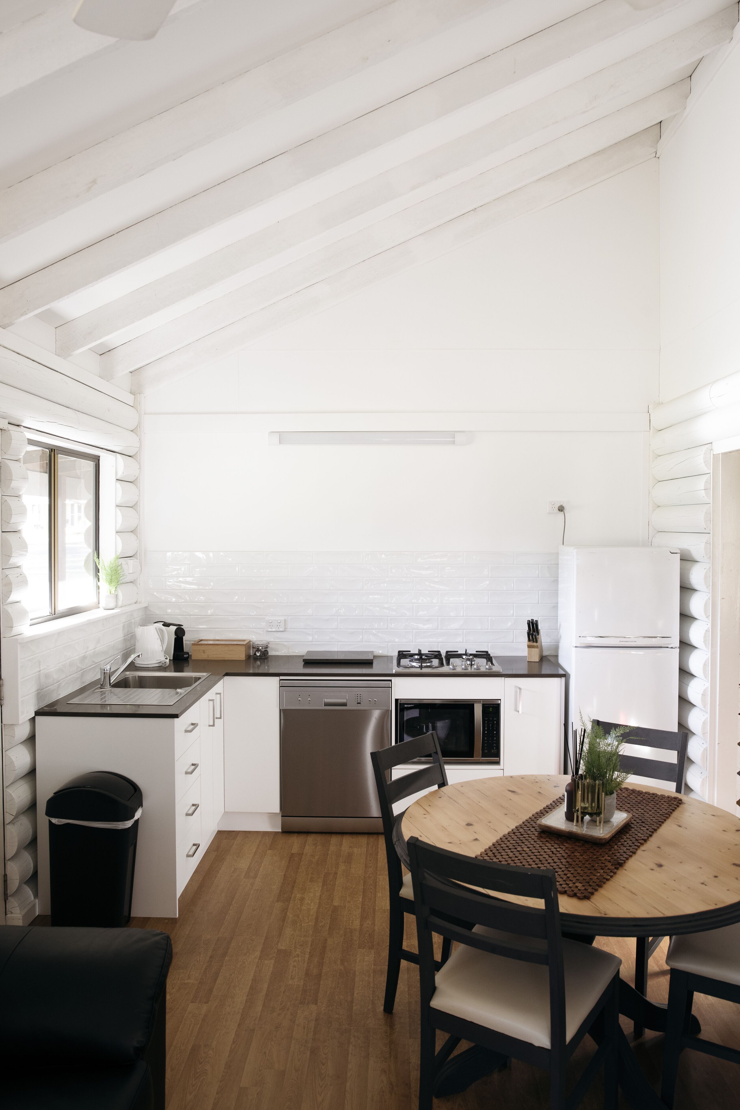 Une cuisine moderne avec des meubles blancs, une table à manger en bois et une poubelle noire.