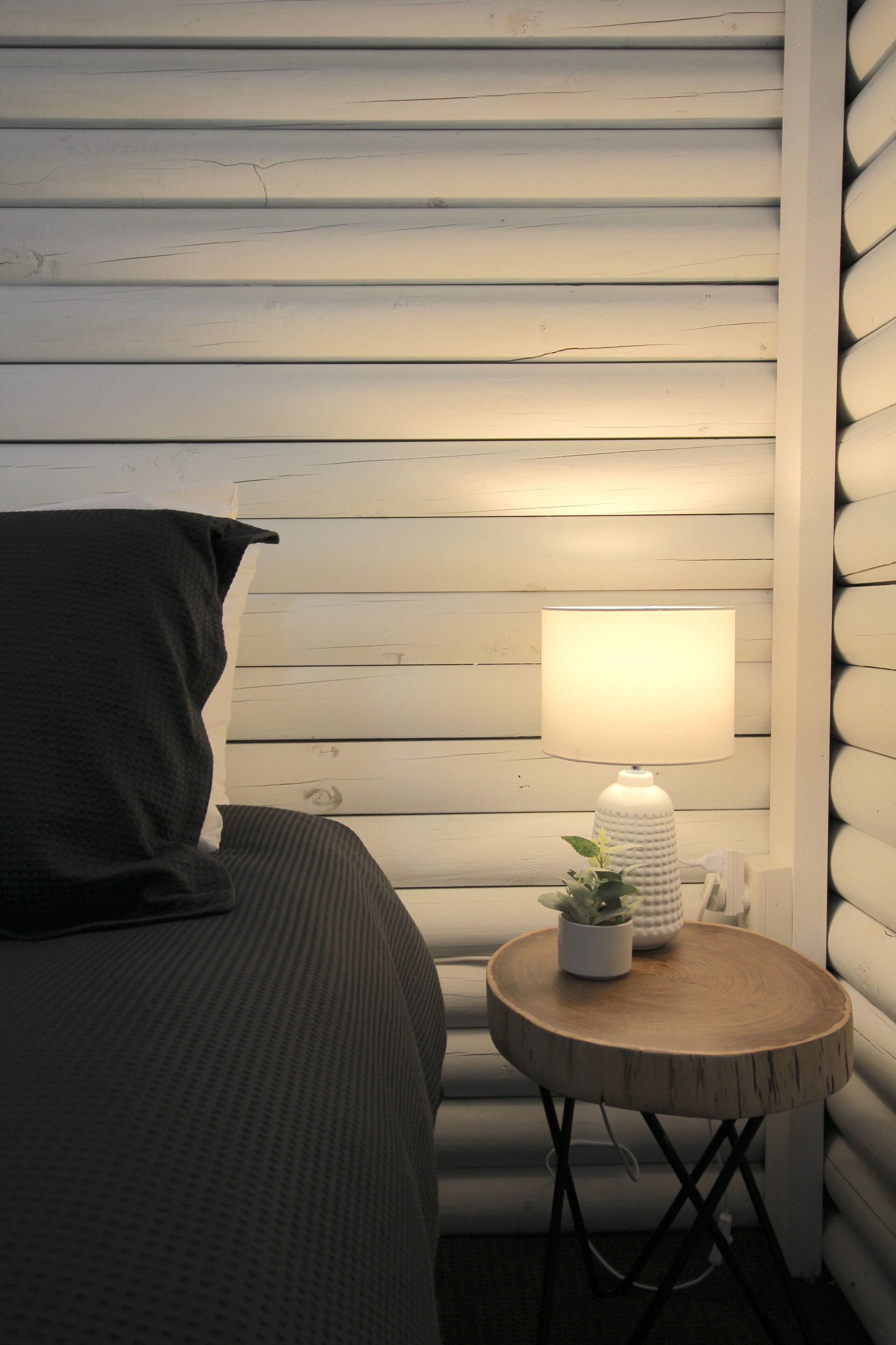 A bedroom with a bed, a bedside table with a lamp, and a wall with horizontal wooden panels.