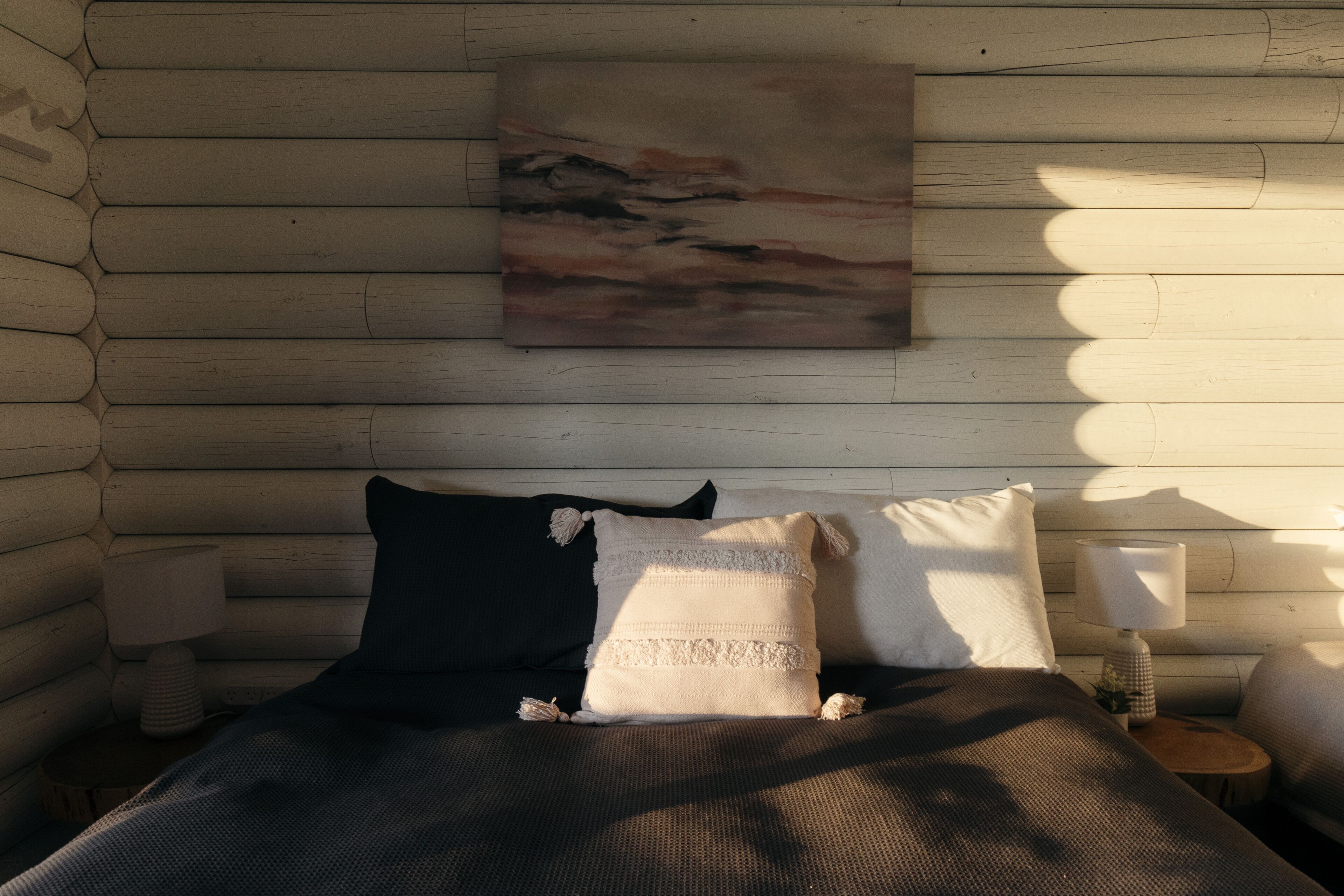 Acogedora habitación tipo cabaña de madera, con cama, almohadas, mesita de noche y lámpara.