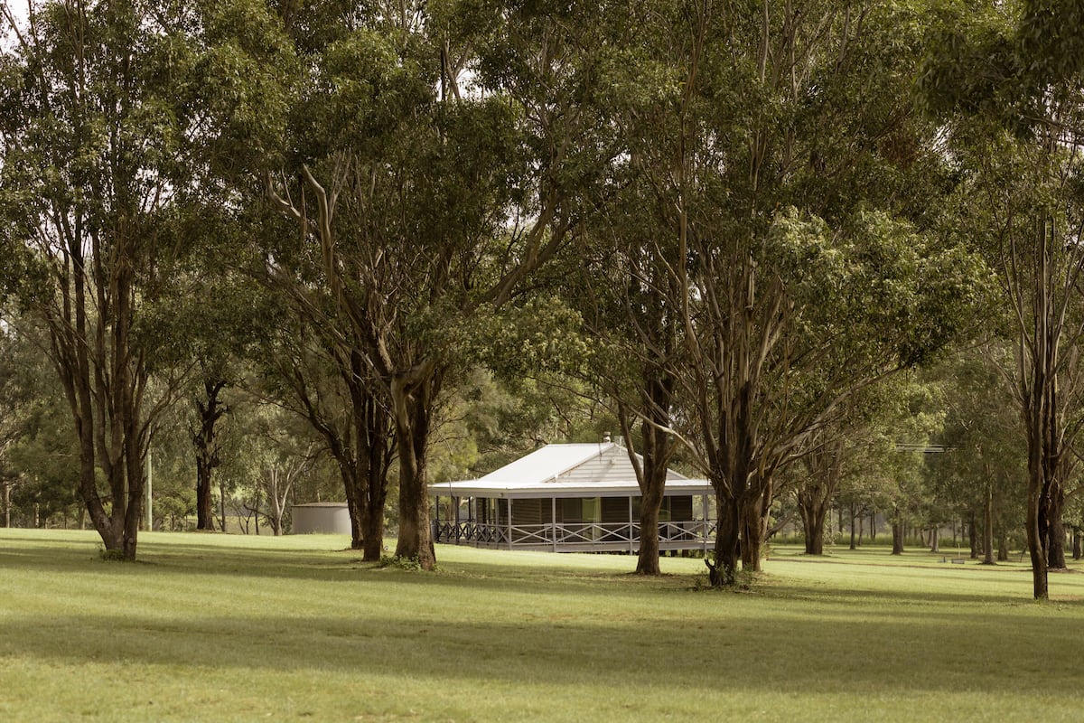 A building with a covered porch surrounded by trees in a grassy area.