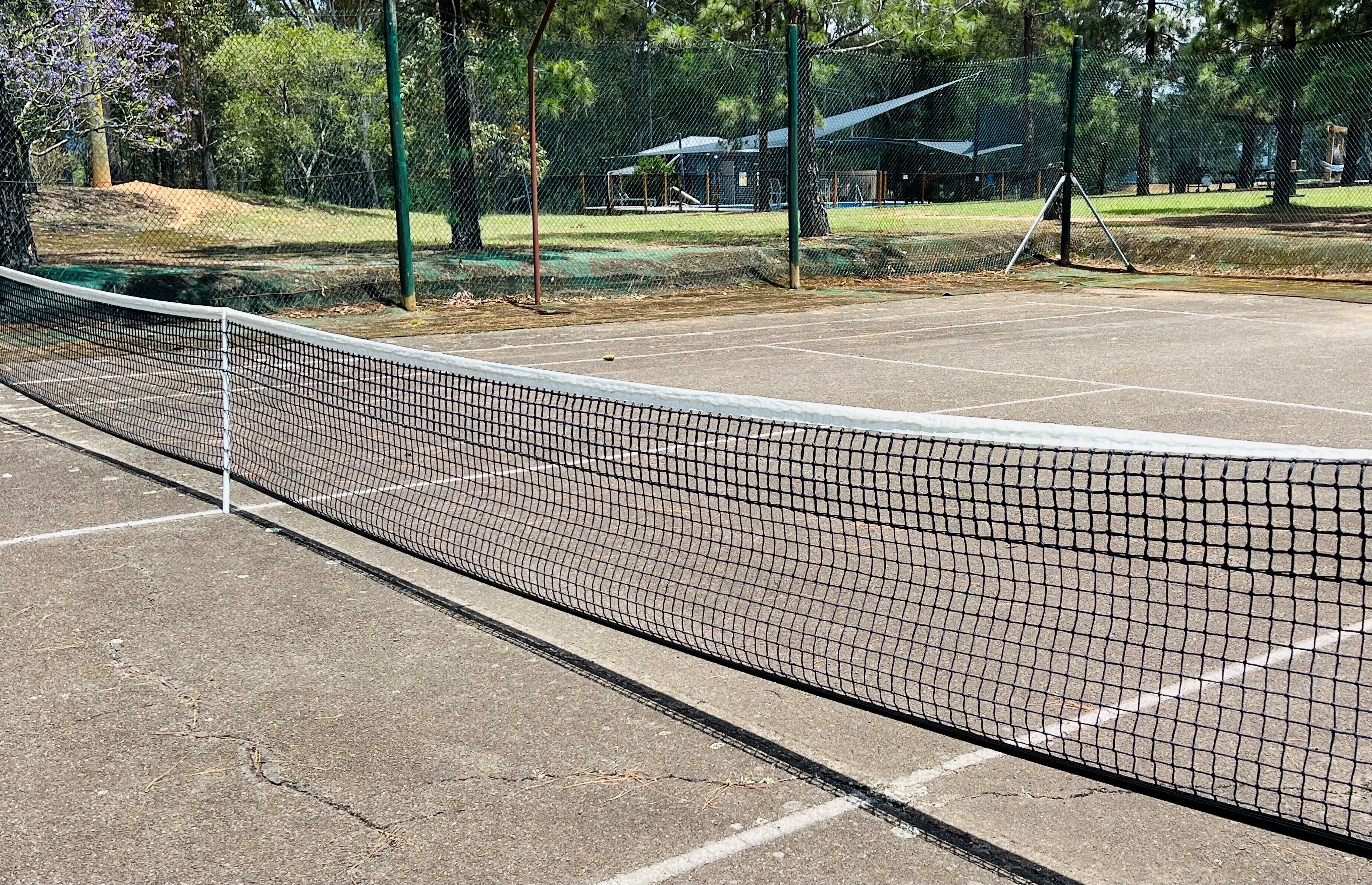Cancha de tenis con una red, rodeada de árboles y una valla.