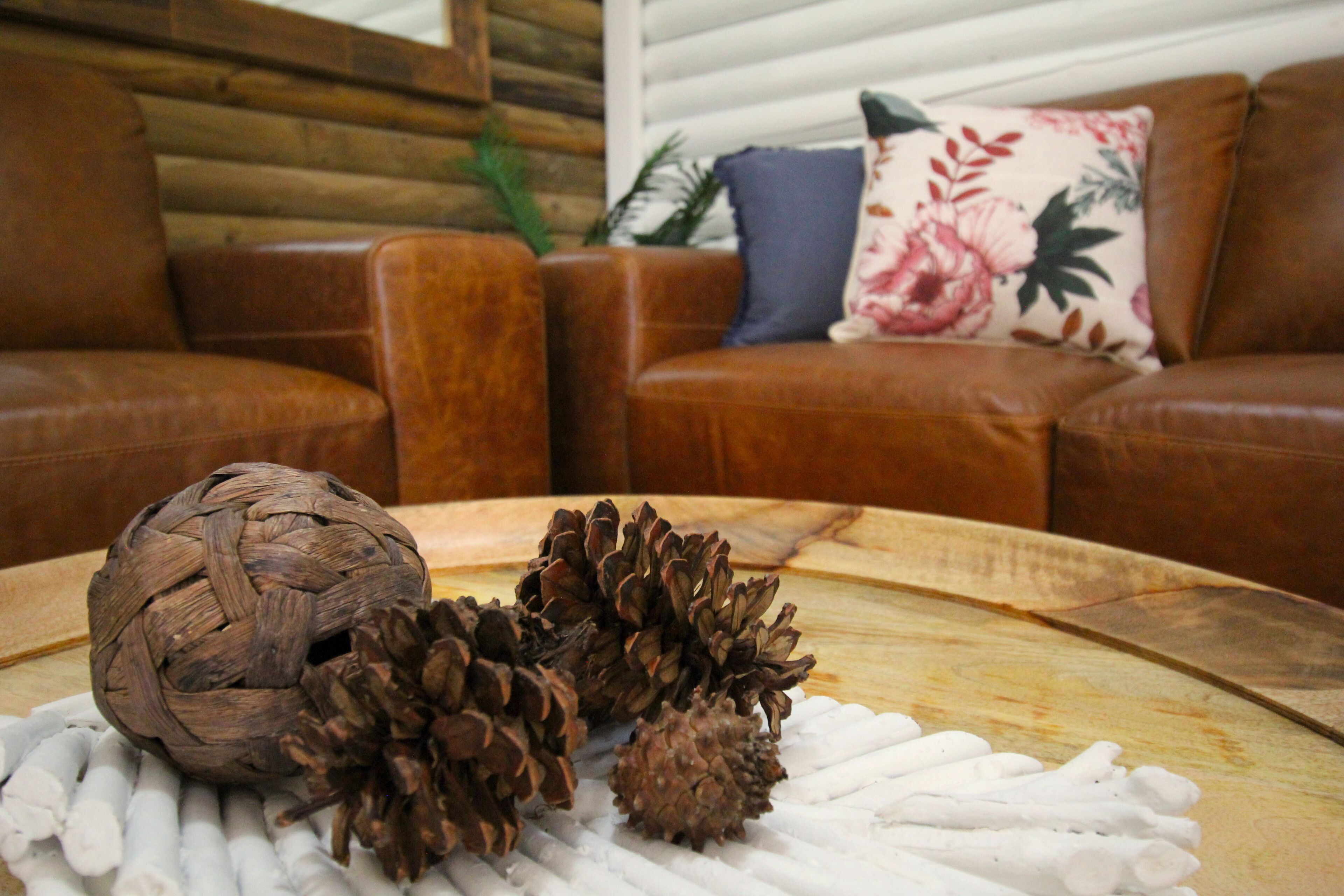 Una mesa de madera con piñas y una bola tejida, un sofá de cuero marrón y un cojín floral.
