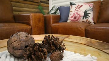 Una mesa de madera con piñas y una bola tejida, un sofá de cuero marrón y un cojín floral.