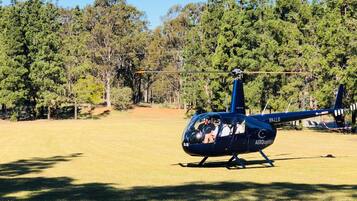A blue helicopter with the registration VH-LLG parked on a grassy field surrounded by trees.