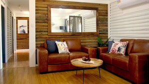 Una sala de estar con un sofá de cuero marrón, un espejo con marco de madera y una pequeña mesa redonda con un objeto decorativo.