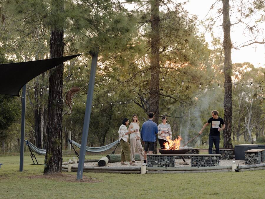 Un grupo de personas reunidas alrededor de un brasero en un parque, con hamacas y mesas de picnic.