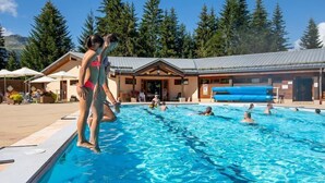 A swimming pool with people in it, surrounded by trees and a building with a sloped roof. - Sleeps 5! Mountain Escape in Valmorel | 1BR Apt (Doucy)