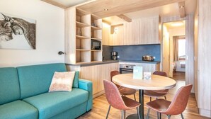 A modern kitchen with wooden cabinets, a dining table with chairs, and a teal sofa with a cushion. - Sleeps 5! Mountain Escape in Valmorel | 1BR Apt (Doucy)