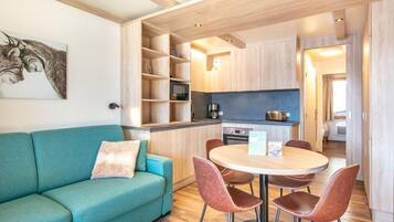 Une cuisine moderne avec des meubles en bois, une table à manger avec des chaises et un canapé turquoise agrémenté d’un coussin.