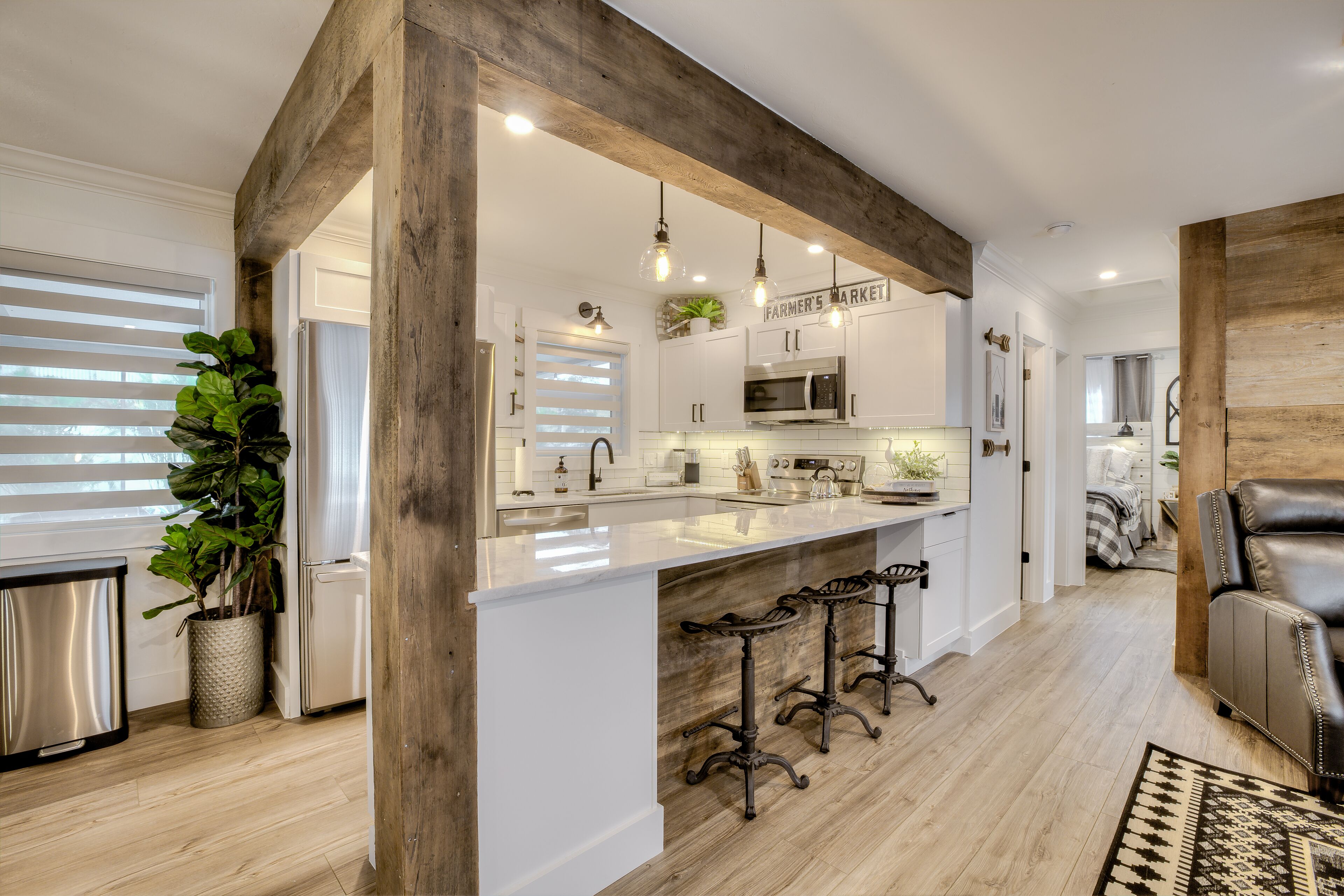 A modern kitchen with white cabinetry, a large island with bar stools, and wooden beams.