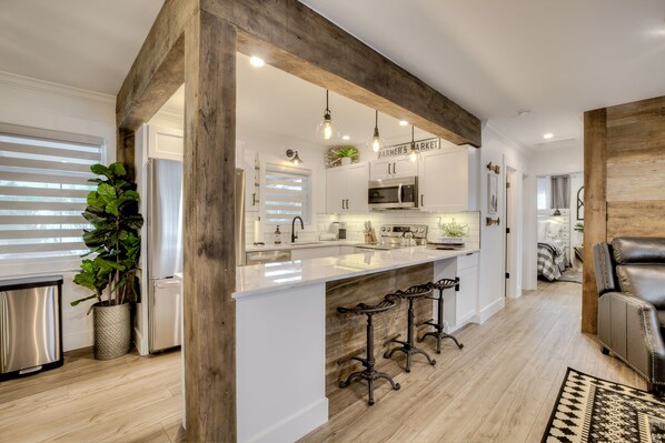 A modern kitchen with white cabinetry, a large island with bar stools, and wooden beams.
