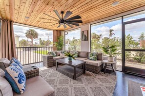 A spacious balcony with a ceiling fan, wicker furniture, and a view of palm trees and a parking lot.