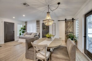 A dining area with a round table, cushioned chairs, a chandelier, and a view of the outdoors through a sliding door.