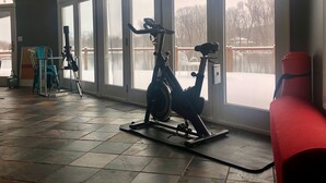 A gym with stationary bikes and a red chair, large windows, and a tiled floor.