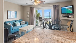 Un salon avec un canapé bleu, une table basse, un téléviseur et un balcon offrant une vue sur l’océan.
