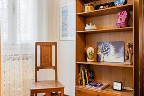 A wooden chair, a bookshelf with decorative items, and a lace curtain. - GuestHost - A Central and Functional Apartment (Bologna)
