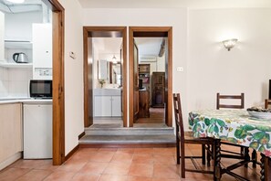A kitchen with a microwave, a coffee maker, and a dishwasher. There is a dining table with chairs and a cactus-patterned tablecloth.