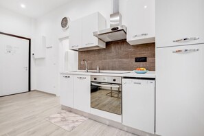 A modern kitchen with white cabinetry, a stainless steel range hood, a built-in oven, and a dishwasher.