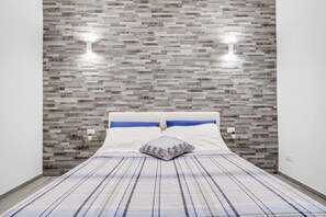 A bedroom with a bed, a patterned bedspread, a pillow, and a wall with a textured, rectangular tile design.